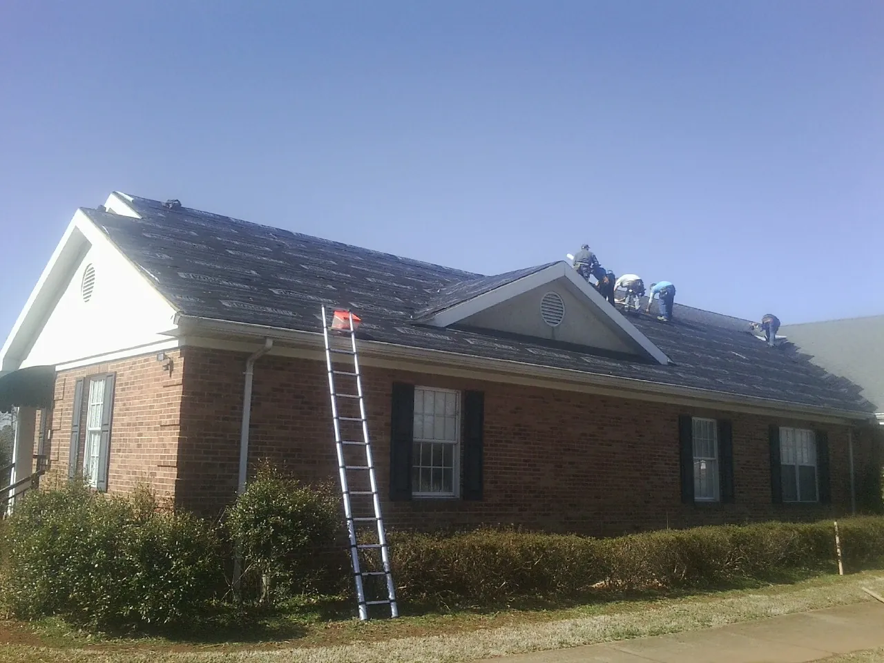 Crew tearing shingles off a brick ranch roof with a ladder set — Metal Roof Repair work by our crew in Lapel
