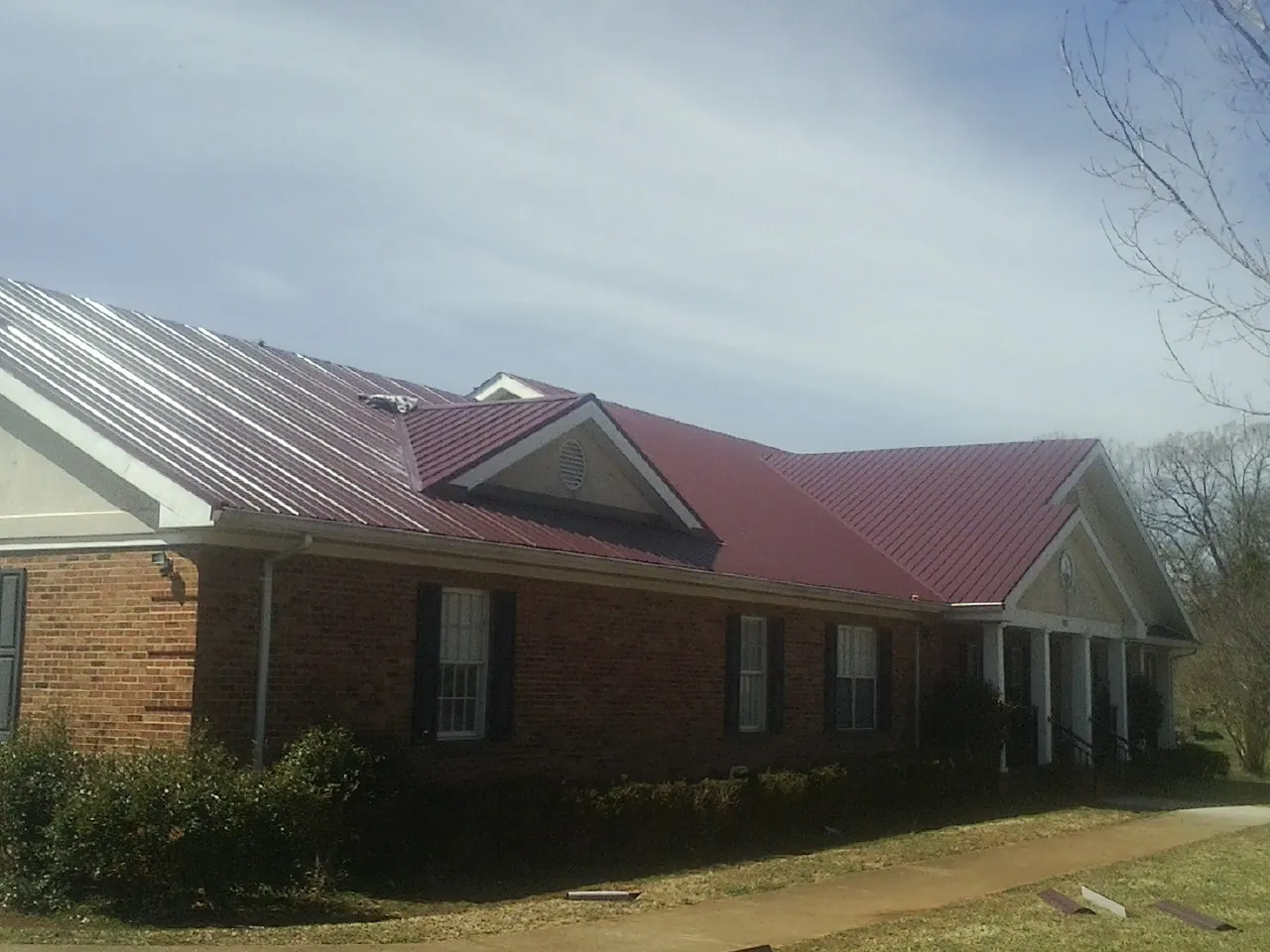 Red metal roof with gabled entries on a long brick building, from a Hail Damage Roof Repair job in Lapel