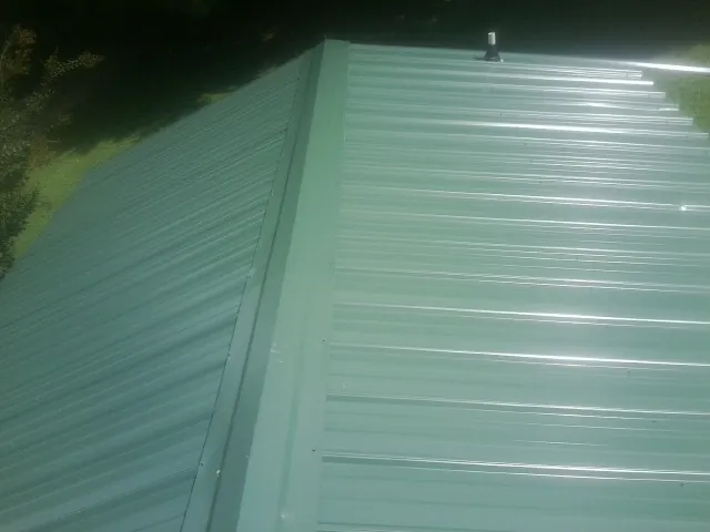 New green metal panels meeting at the ridge of a roof — Flat Roof Repair work by our crew in Lapel
